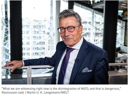 Man in a navy suit and glasses speaks in a bright studio; caption quotes Rasmussen: NATO disintegration is dangerous.